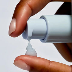 Hand holding a small bottle with a white cap, squeezing out a drop of clear gel onto a white background.