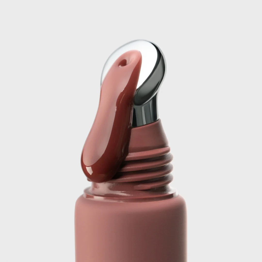 Close-up of a pink lip gloss with a silver applicator on a light gray background