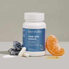 Supplement bottle labeled 'face reality clear skin restore' with a tangerine and rocks on a neutral background