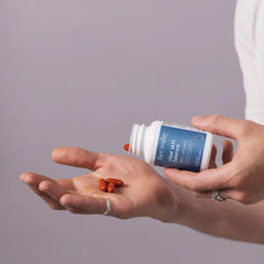 Person holding a supplement bottle and pills on an open palm against a gray background